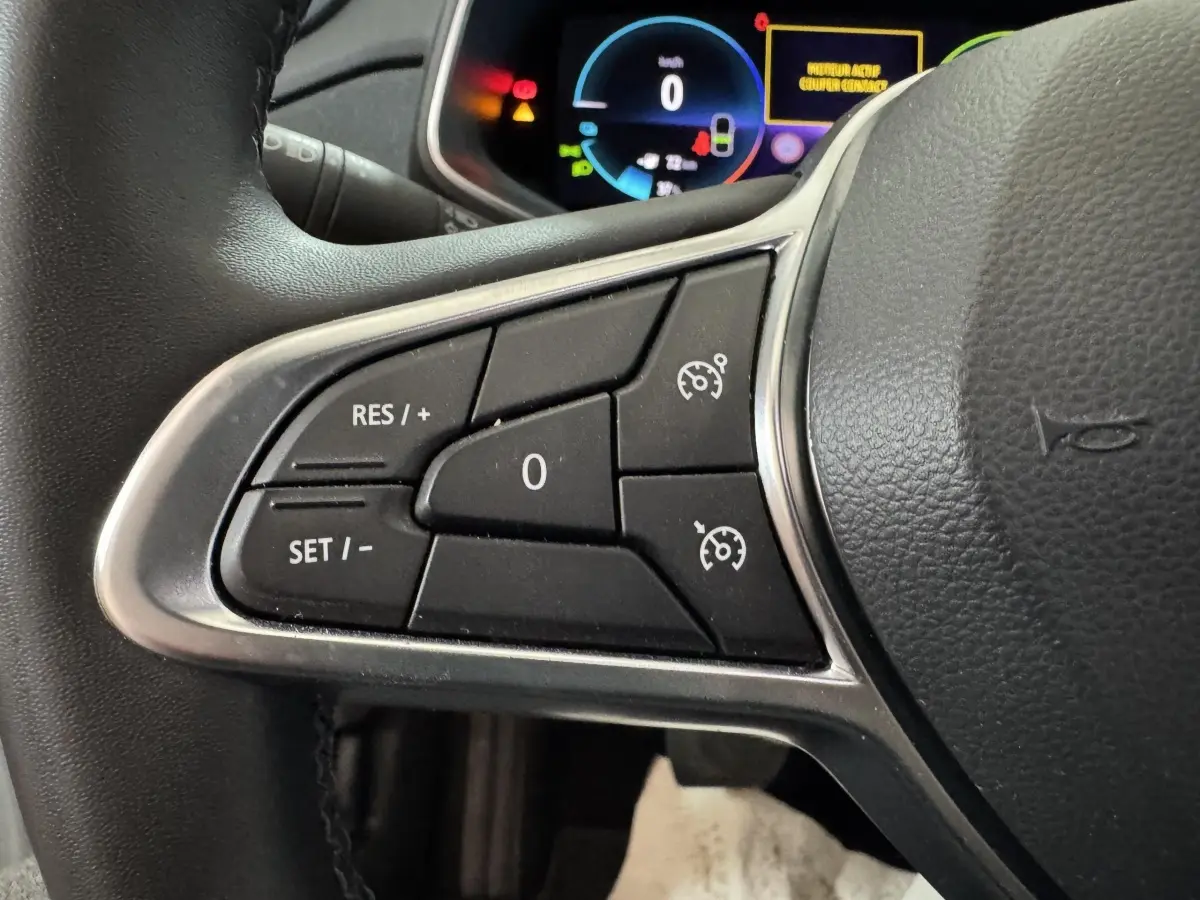 Gros plan sur les commandes du régulateur de vitesse au volant cuir de la Renault ZOE Business blanc 2020.