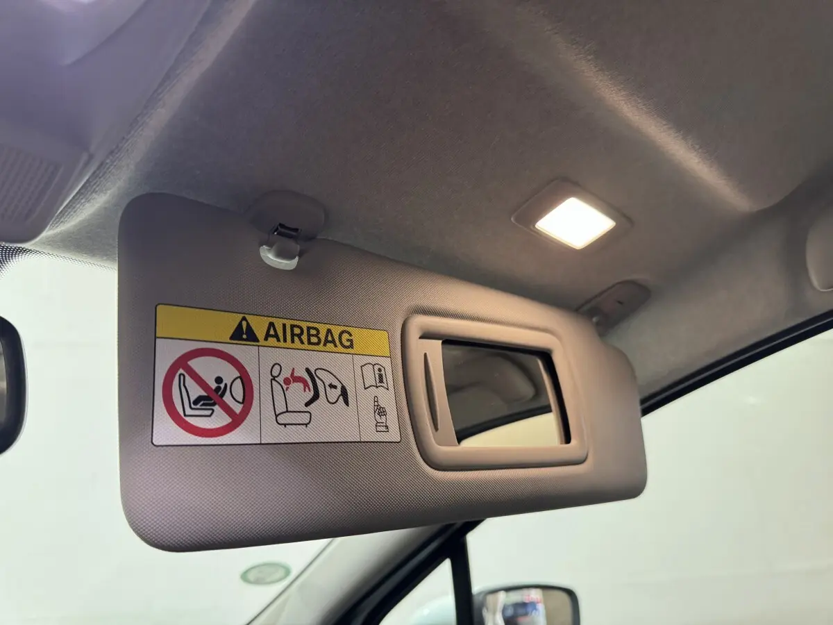 Vue intérieure rapprochée du pare-soleil côté conducteur beige avec miroir et avertissement airbag dans une Renault ZOE blanche 2020.