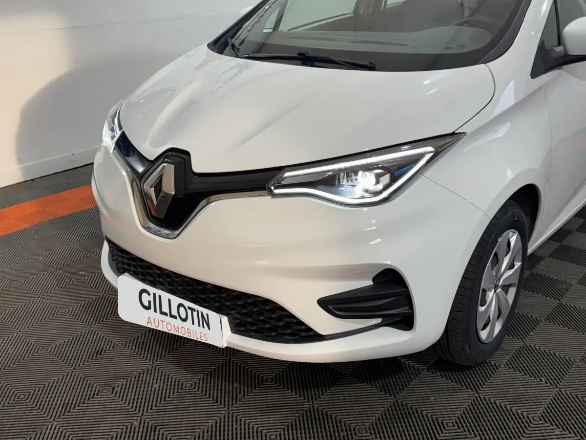 Vue 3/4 avant droit d'une Renault ZOE Business blanche avec phares LED allumés et calandre noire distinctive.