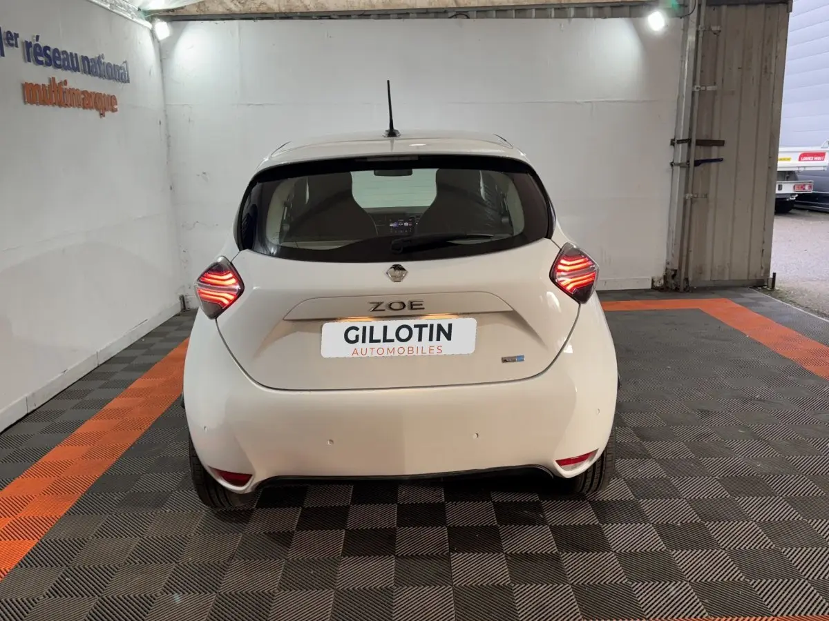 Vue arrière d'une Renault ZOE Business blanche de 2020 avec feux LED allumés, stationnée en intérieur.