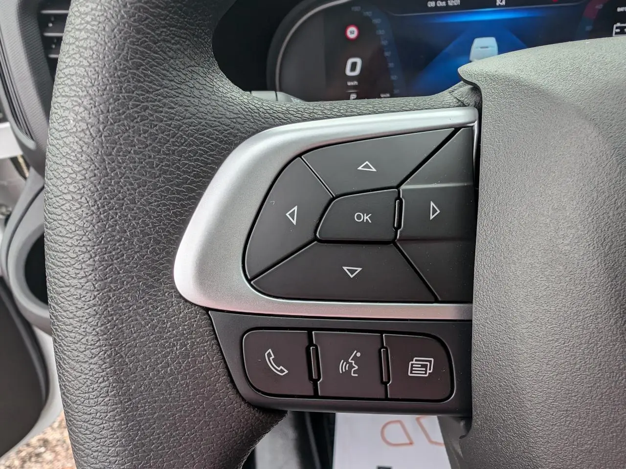 Gros plan sur les commandes multifonctions du volant noir de l’IVECO Daily 35S16 blanc, affichage digital en arrière-plan.