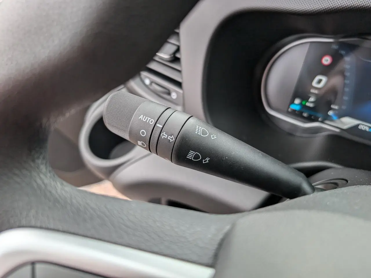 Gros plan sur le commodo noir des phares et clignotants à gauche du volant dans l'habitacle du Iveco Daily blanc.