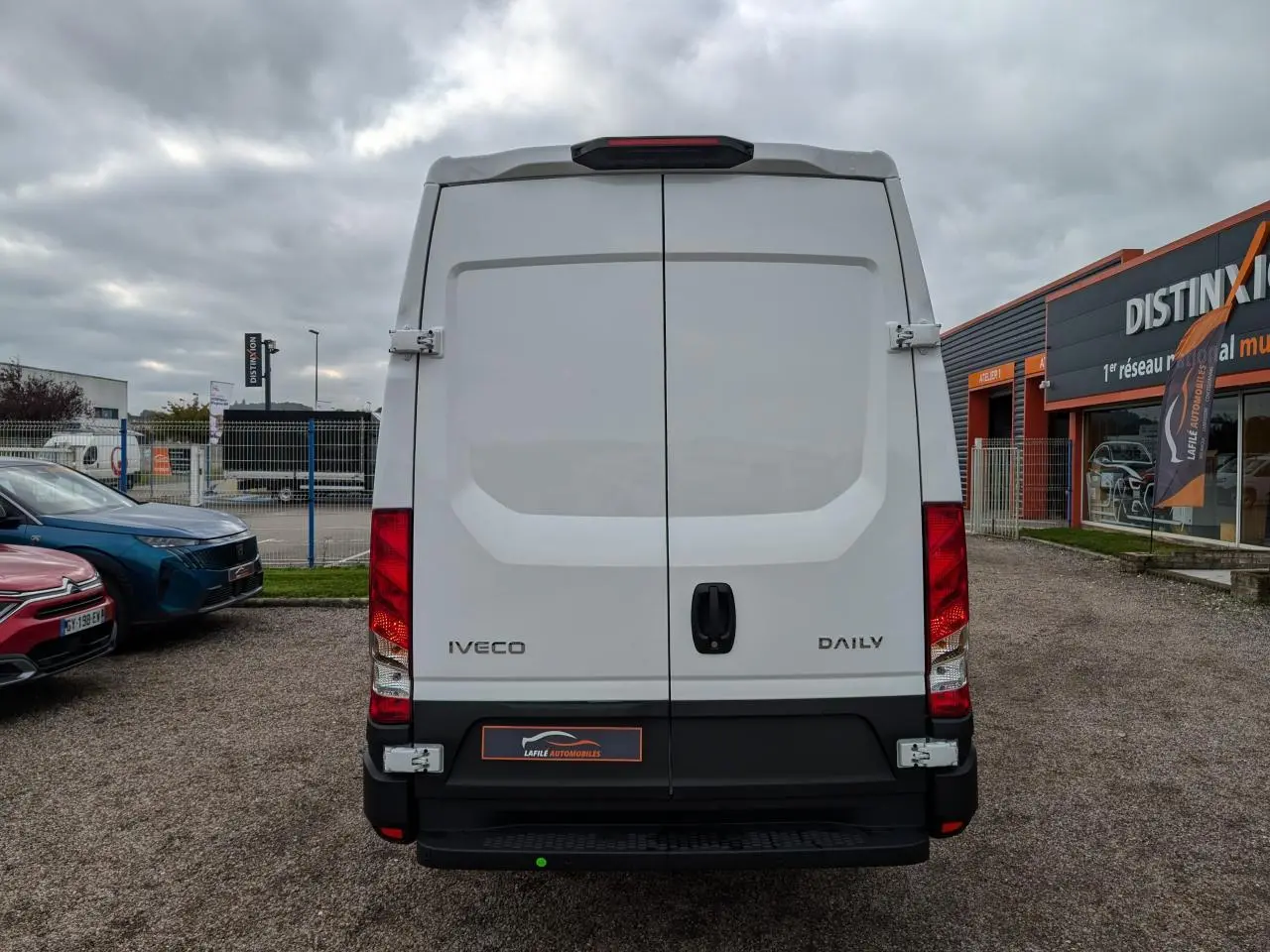 Vue arrière d’un utilitaire Iveco Daily blanc, portes battantes fermées avec poignées noires et feux rouges verticaux.