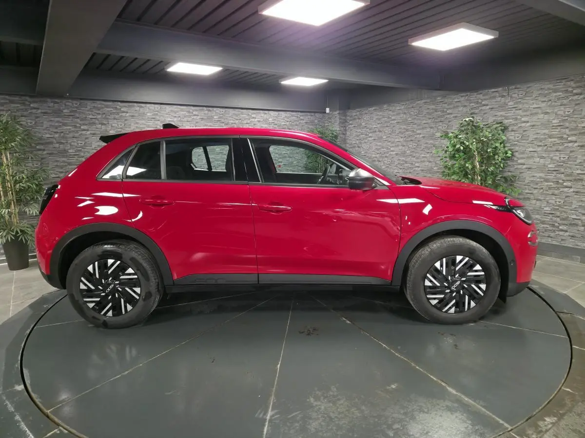 Vue de profil côté gauche d'une FIAT 600 rouge 2024 avec jantes bicolores et coques de rétroviseurs noires.