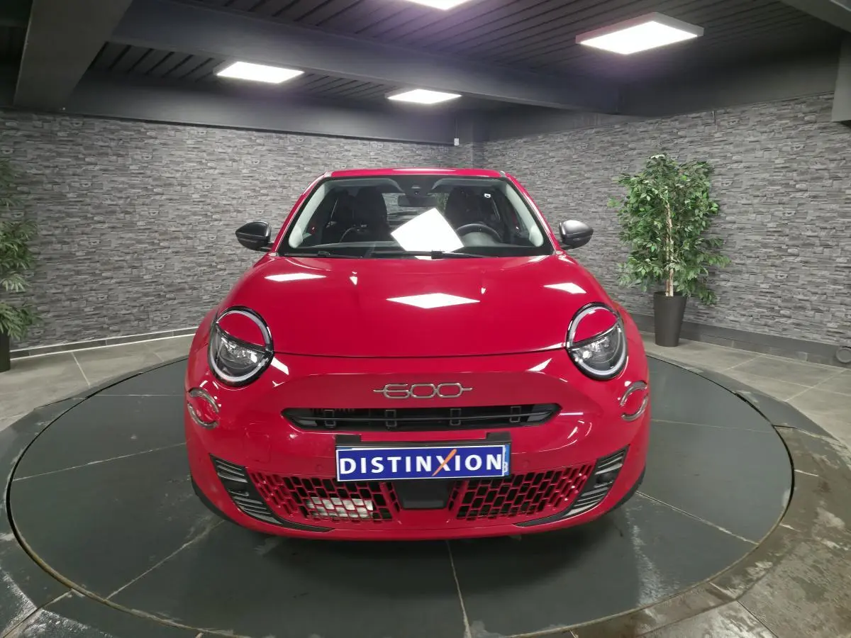 Vue avant d'une FIAT 600 rouge brillante avec logo 600 et calandre noire dans un showroom.