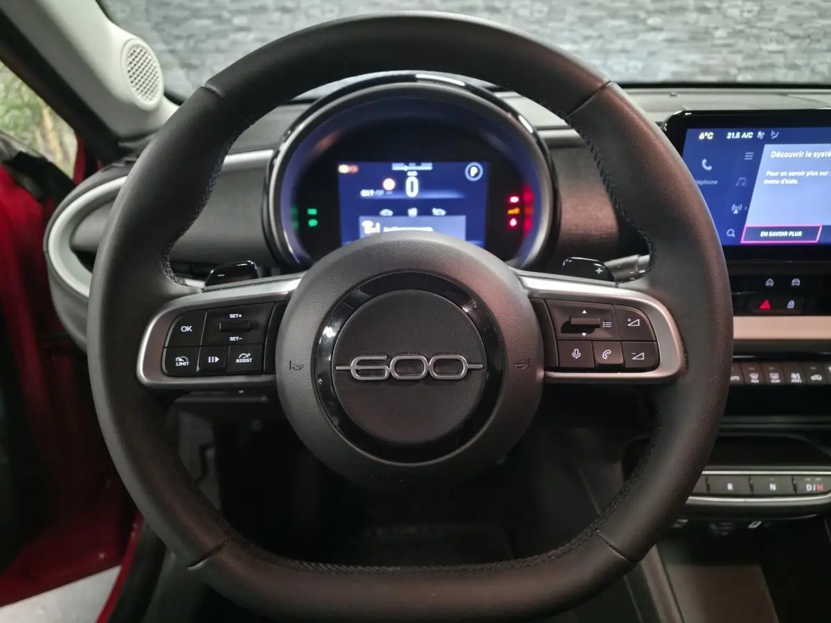 Vue centrée sur le volant noir de la FIAT 600 rouge 2024 avec tableau de bord numérique et écran tactile.