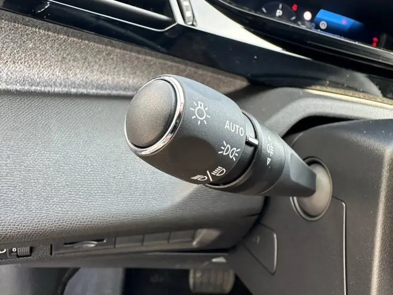 Gros plan sur la commande des phares automatique à gauche du volant dans l'habitacle gris d'une Peugeot 308 2025.