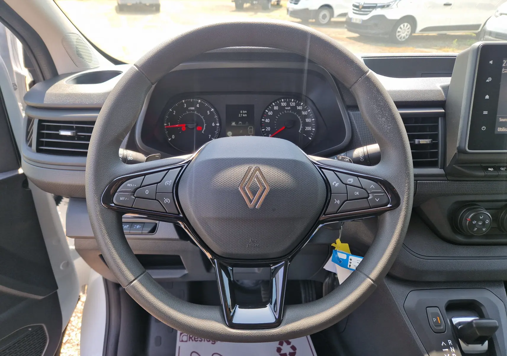 Vue intérieure centrée sur le volant noir du Renault Trafic Fourgon blanc, avec tableau de bord et écran tactile visible.
