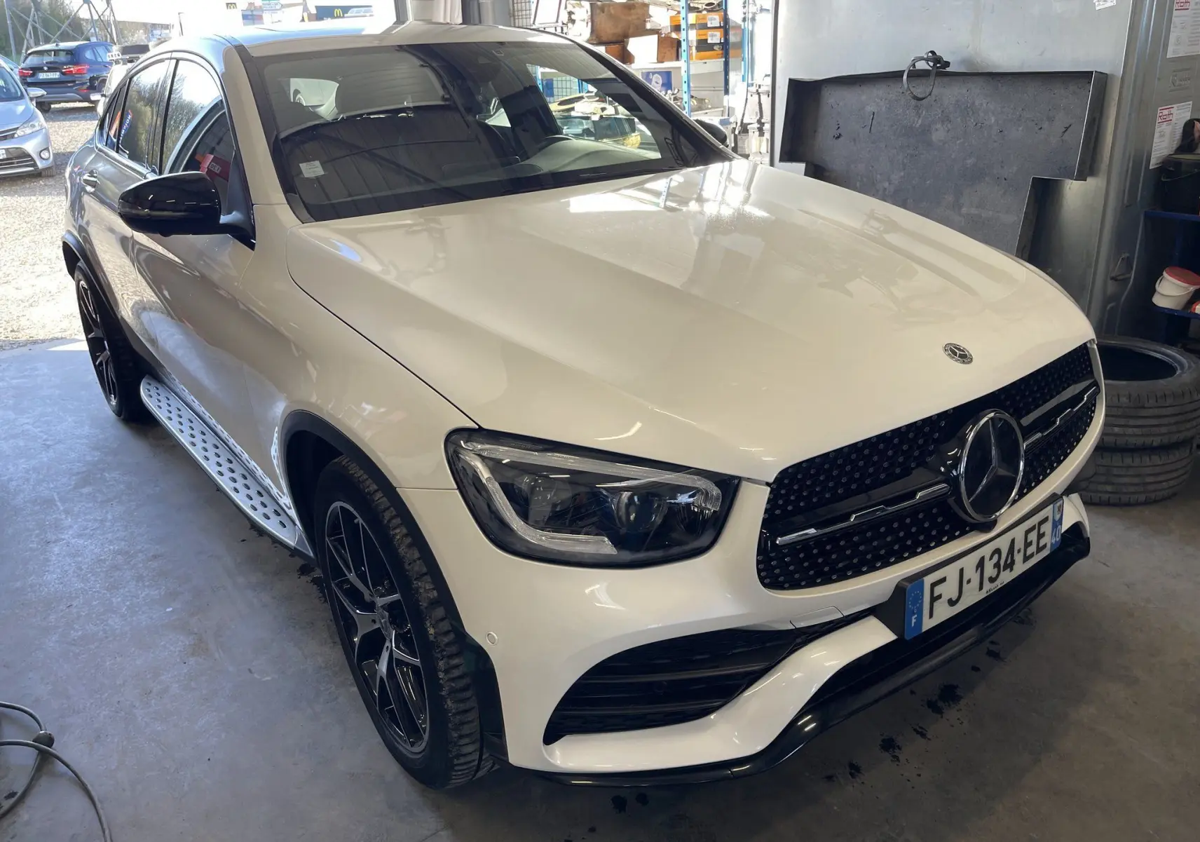 Mercedes GLC Coupé blanc vu en 3/4 avant droit avec calandre AMG noire et jantes noires dans un garage.