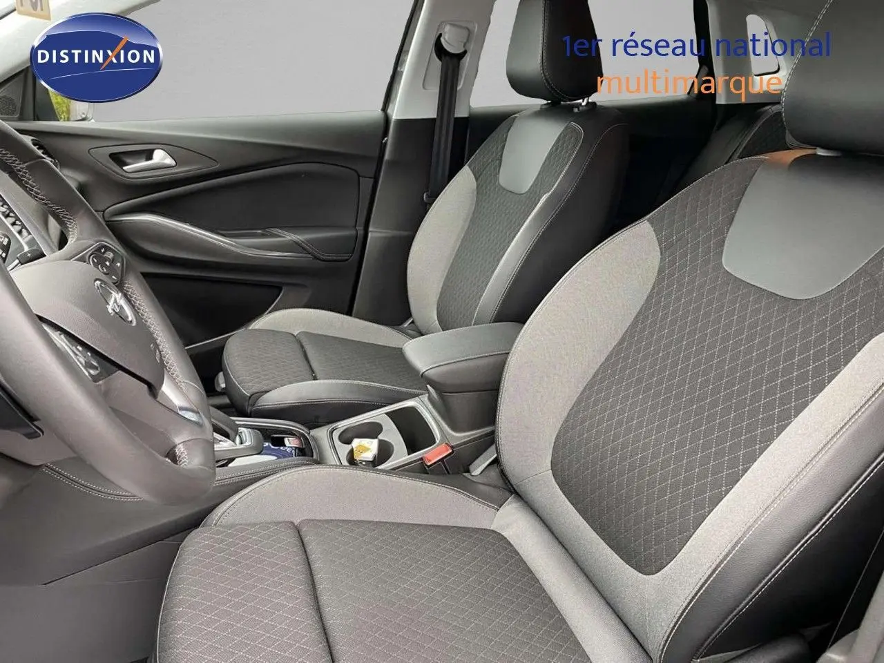Vue intérieure côté gauche de l’Opel Grandland X 1.6 Hybrid Turbo 2021 avec sièges tissu noir et gris à motifs losanges.