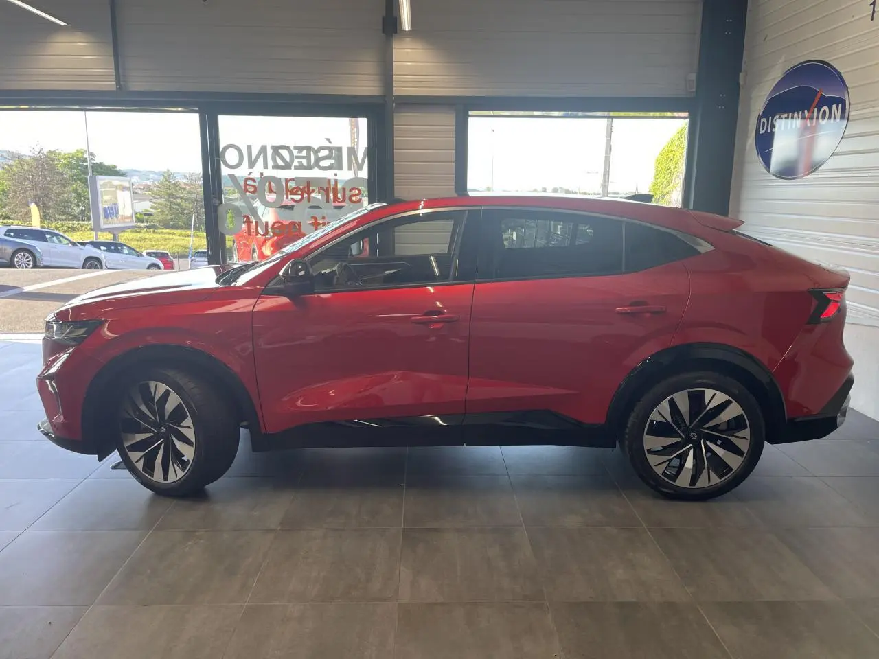 Vue de profil côté gauche d'une Renault Rafale rouge avec toit noir et jantes alliage noires en intérieur showroom.