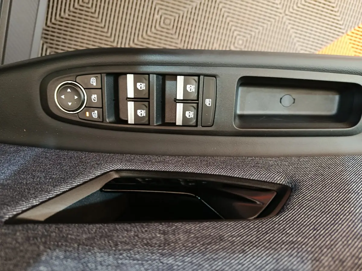 Gros plan sur les commandes de lève-vitres et rétroviseurs électriques sur la porte côté conducteur d'une Renault R5 blanche.