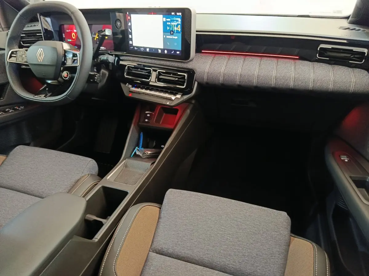 Vue intérieure avant droite de la Renault R5 Techno 150 ch 2025, avec tableau de bord tactile et éclairage d'ambiance rouge.