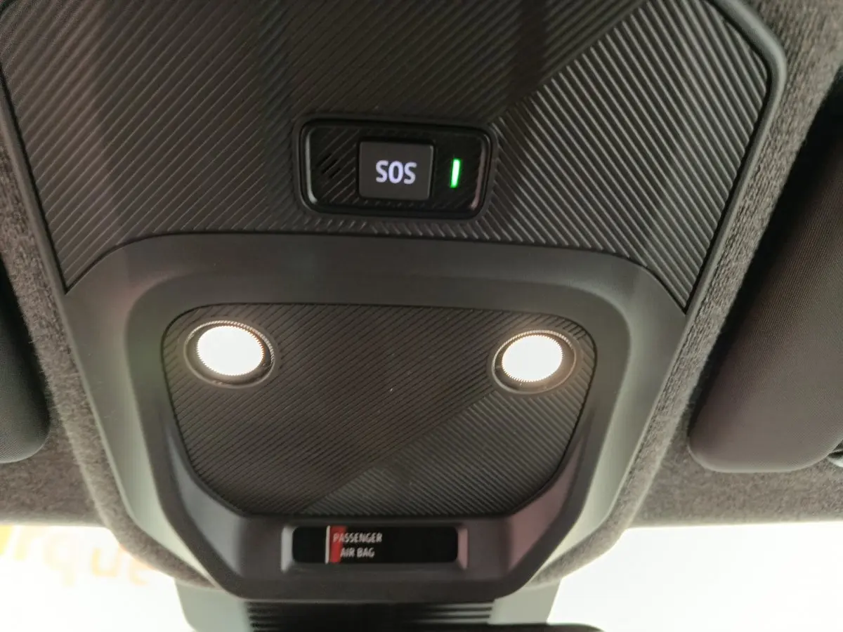 Vue en contre-plongée du plafonnier intérieur noir avec bouton SOS éclairé et deux lampes allumées dans une Renault R5 blanche électrique.