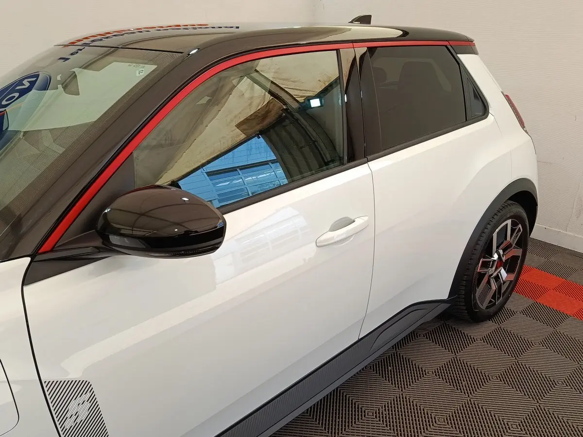 Vue côté droit arrière d'une Renault R5 Techno blanche avec toit noir, rétroviseur noir et jante stylisée rouge et noire.