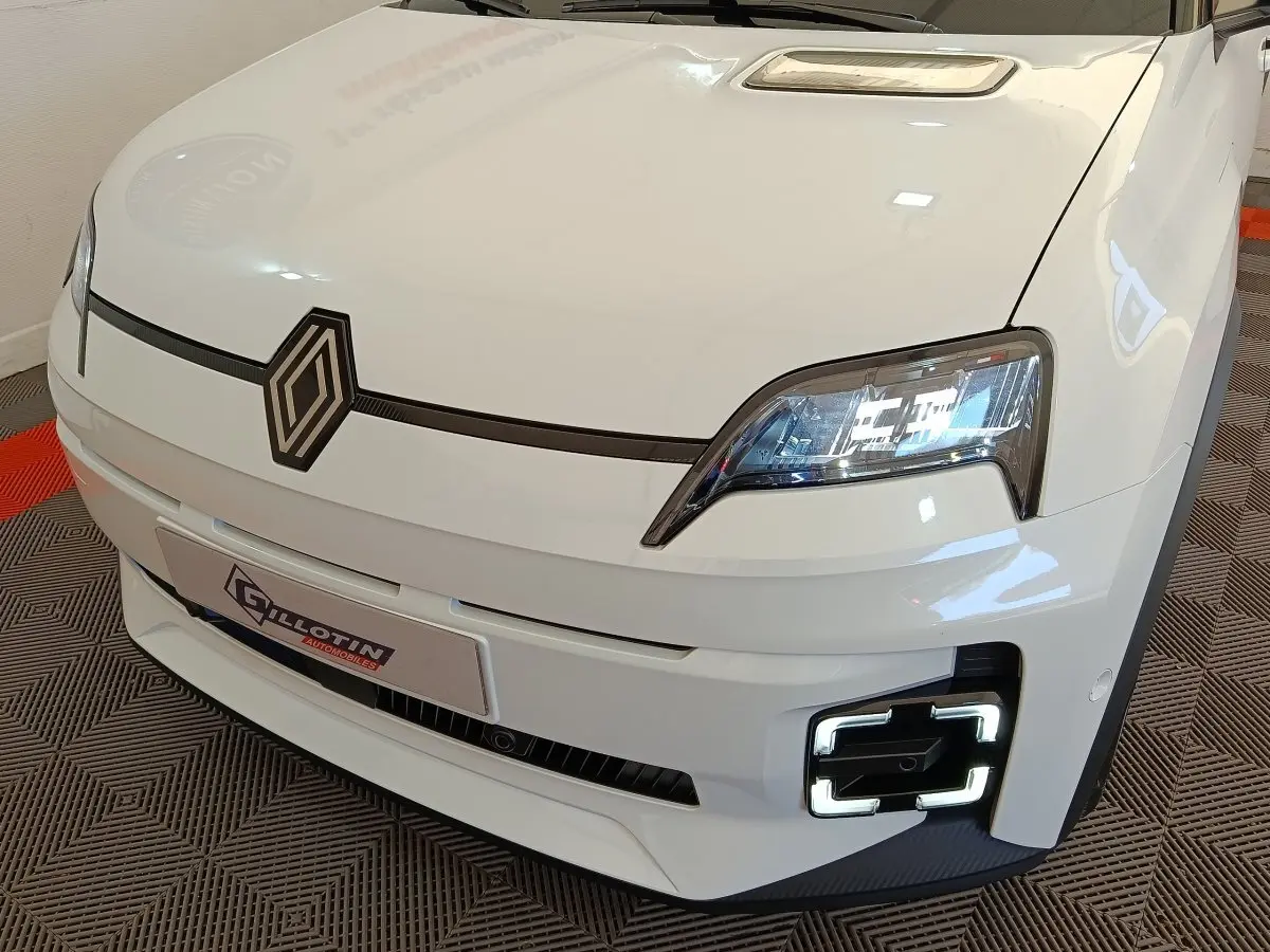 Vue 3/4 avant droit de la Renault R5 Techno blanche 2025 avec phares LED et signature lumineuse carrée distinctive.