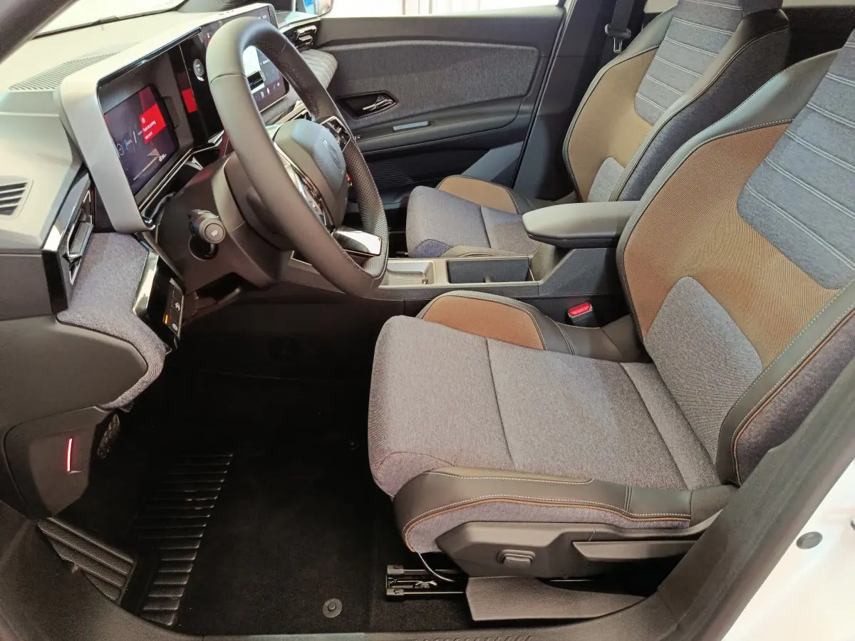 Vue intérieure côté conducteur de la Renault R5 Techno 2025, sièges tissu gris et brun avec volant multifonctions.