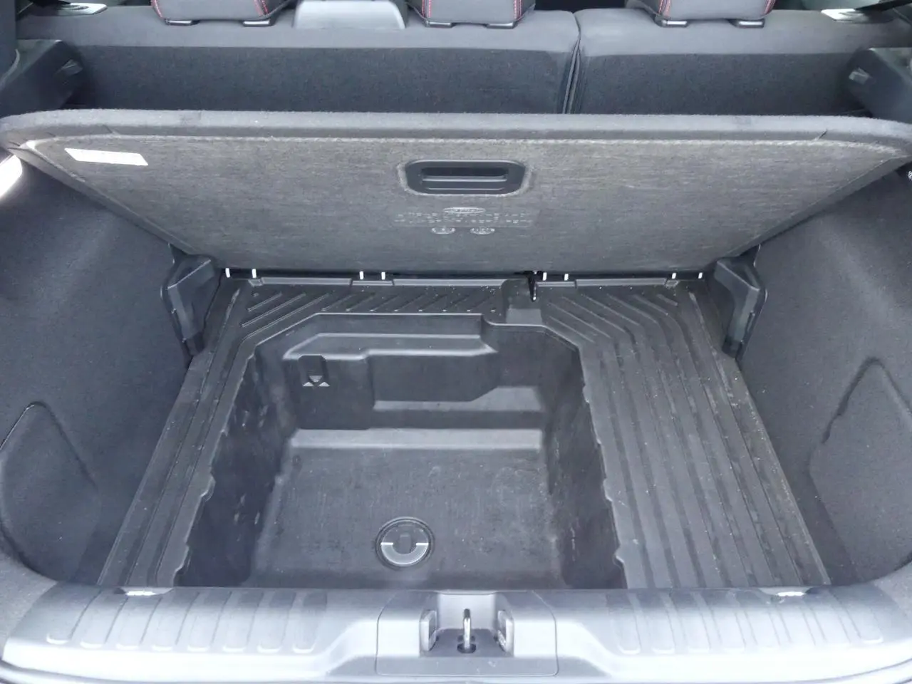 Vue plongeante sur le coffre ouvert du Ford Puma blanc, montrant le compartiment de rangement sous plancher.