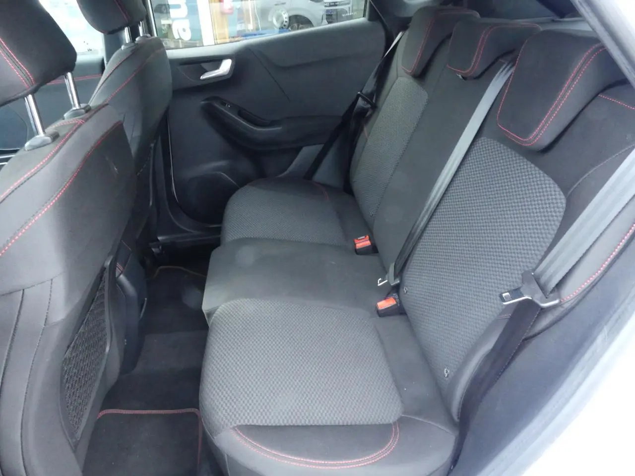 Vue intérieure du côté gauche sur la banquette arrière noire avec surpiqûres rouges du Ford Puma ST Line blanc.