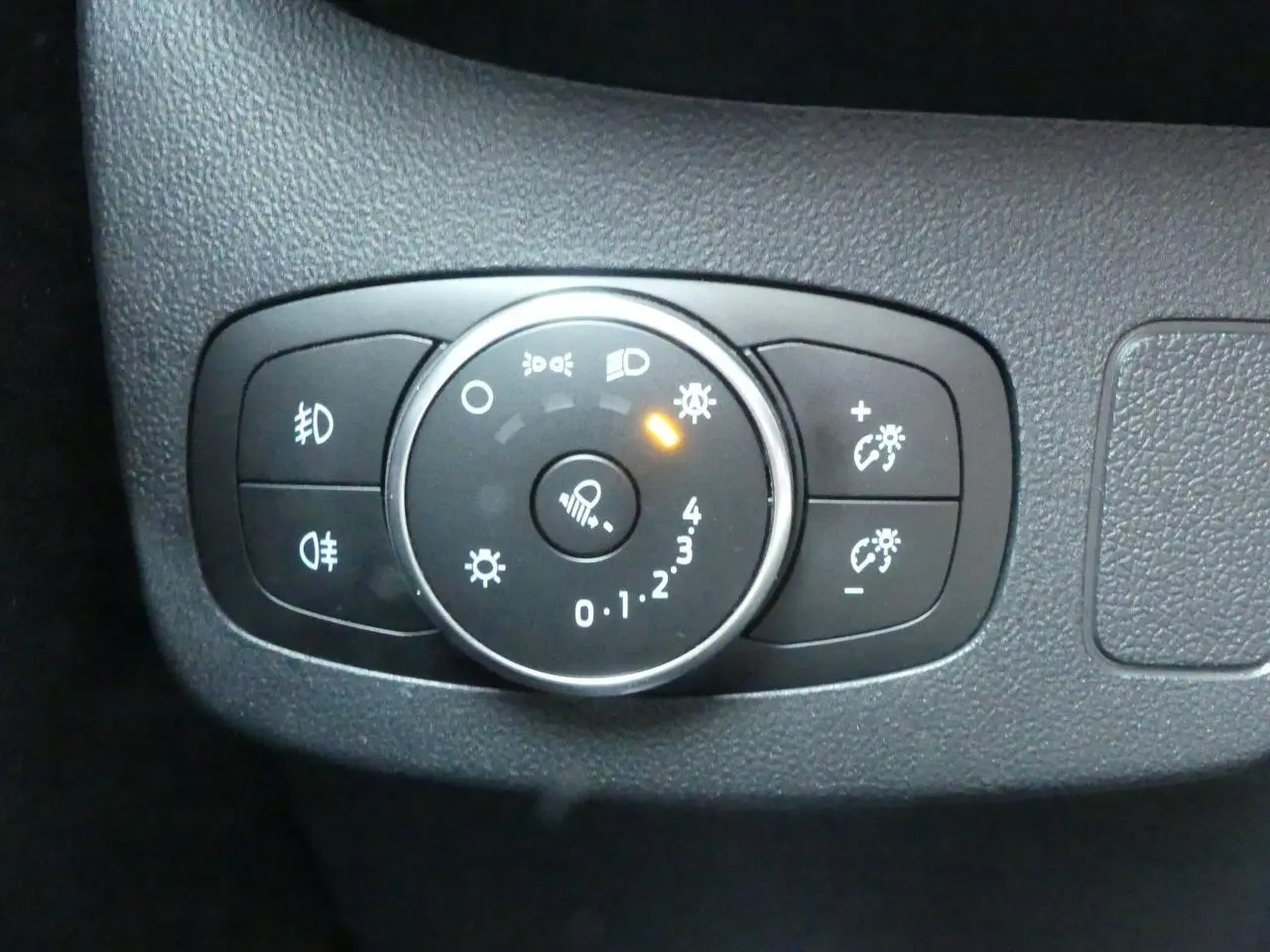 Gros plan sur la molette de réglage des phares et des feux du tableau de bord noir du Ford Puma blanc.