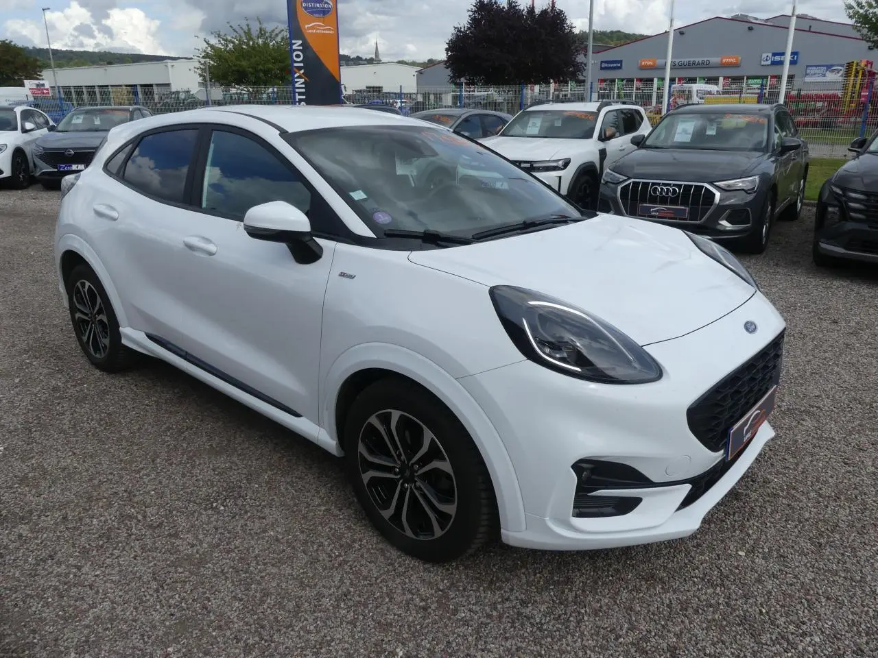 Ford Puma blanc en 3/4 avant droit avec jantes alliage noires et vitres arrière surteintées sur parking extérieur.