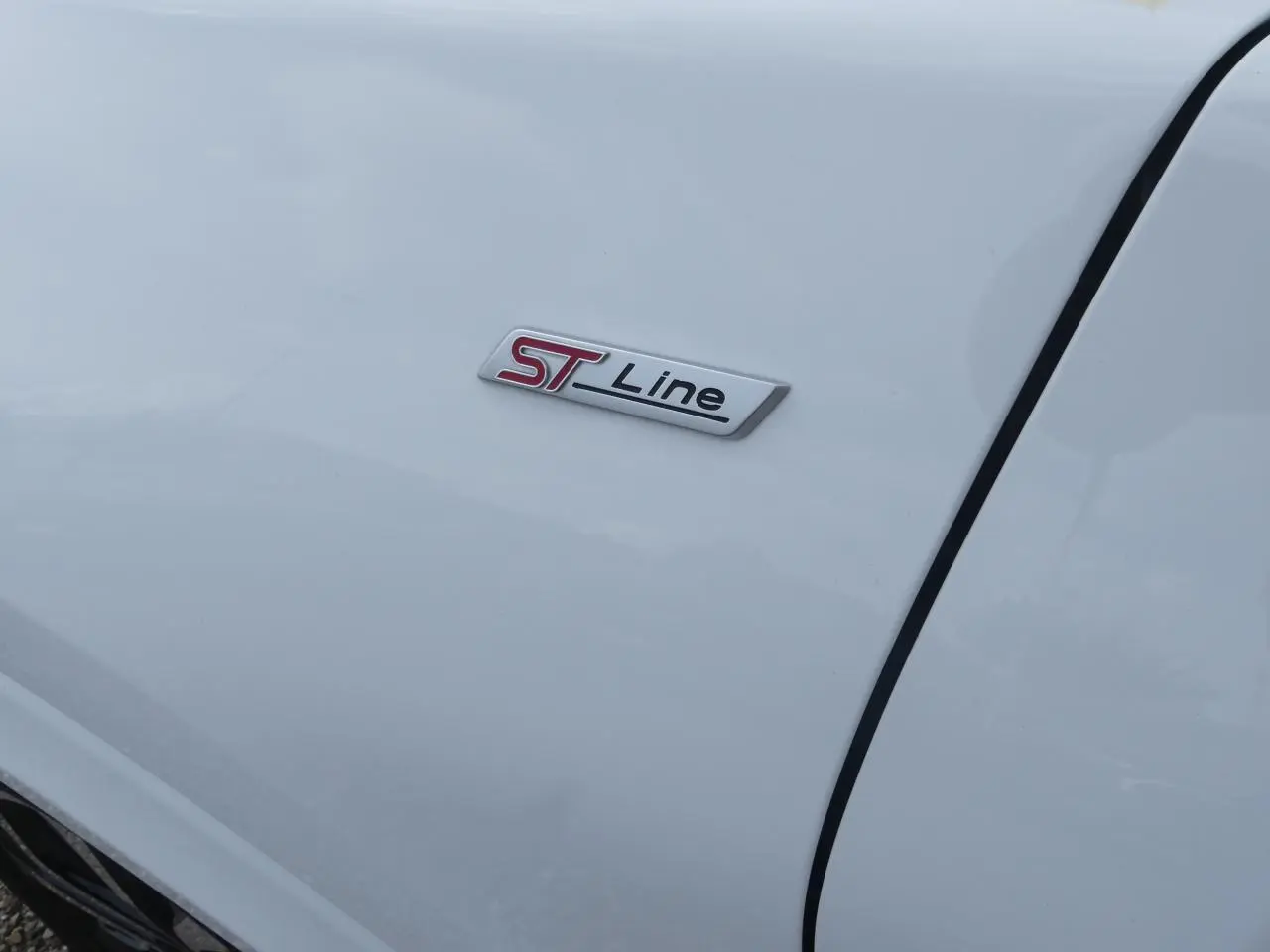 Gros plan sur l'écusson ST-Line rouge et noir sur la carrosserie blanche d'une Ford Puma 2020.