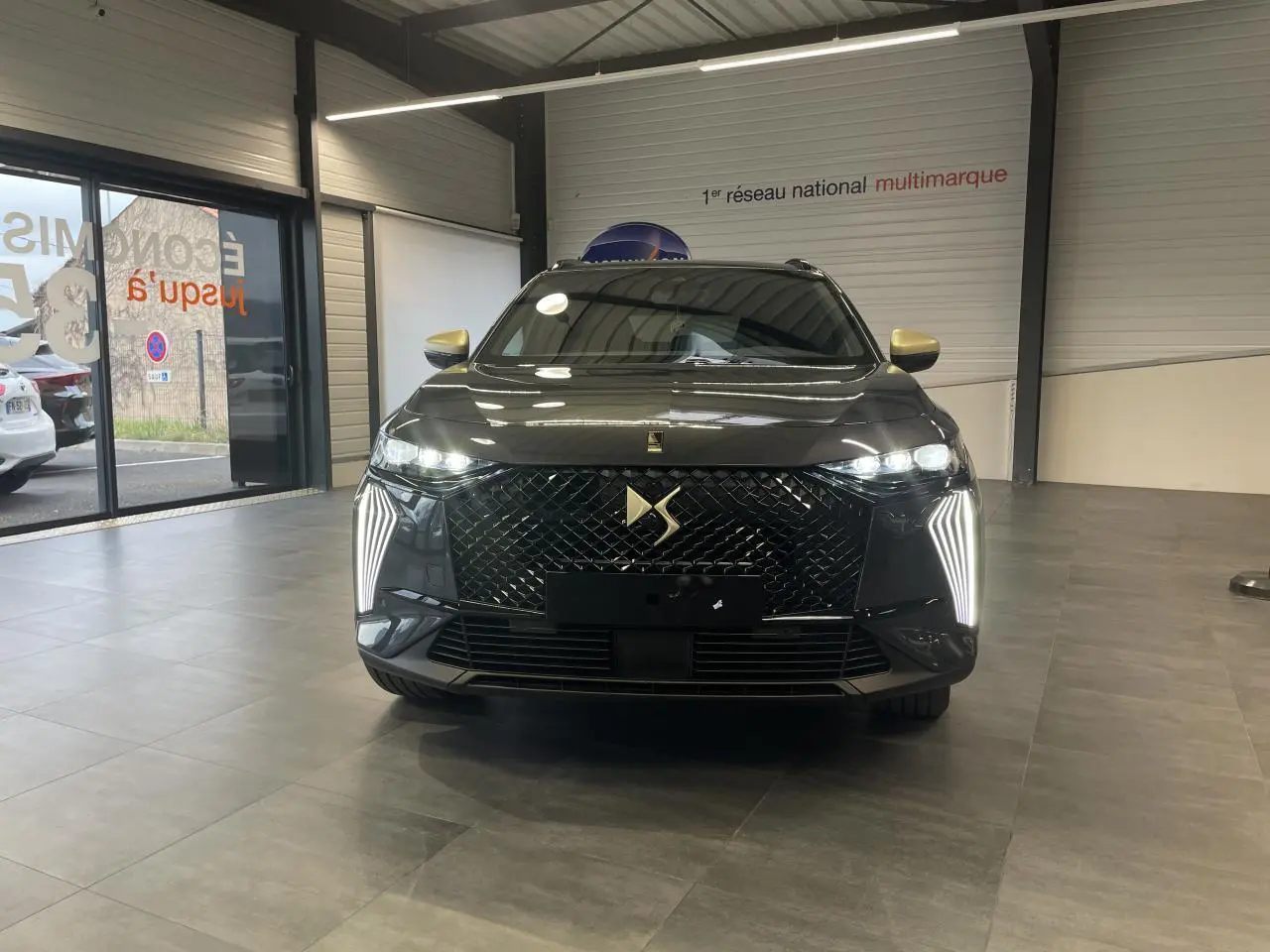 Vue frontale du DS7 Crossback gris titanium avec calandre DS Wings noir brillant et feux LED verticaux allumés.