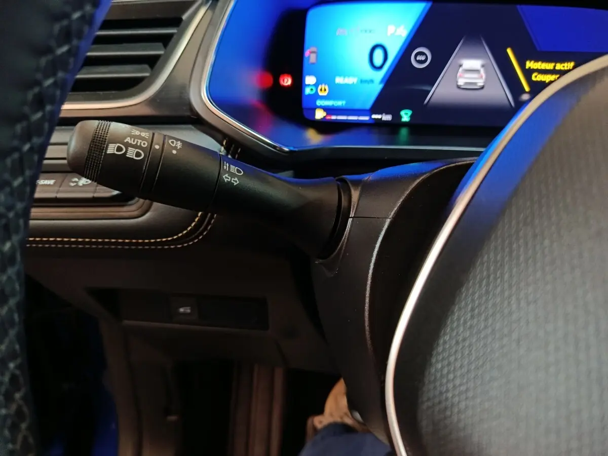 Gros plan sur la manette de phares et clignotants à gauche du volant du Renault Symbioz bleu, tableau de bord numérique visible.