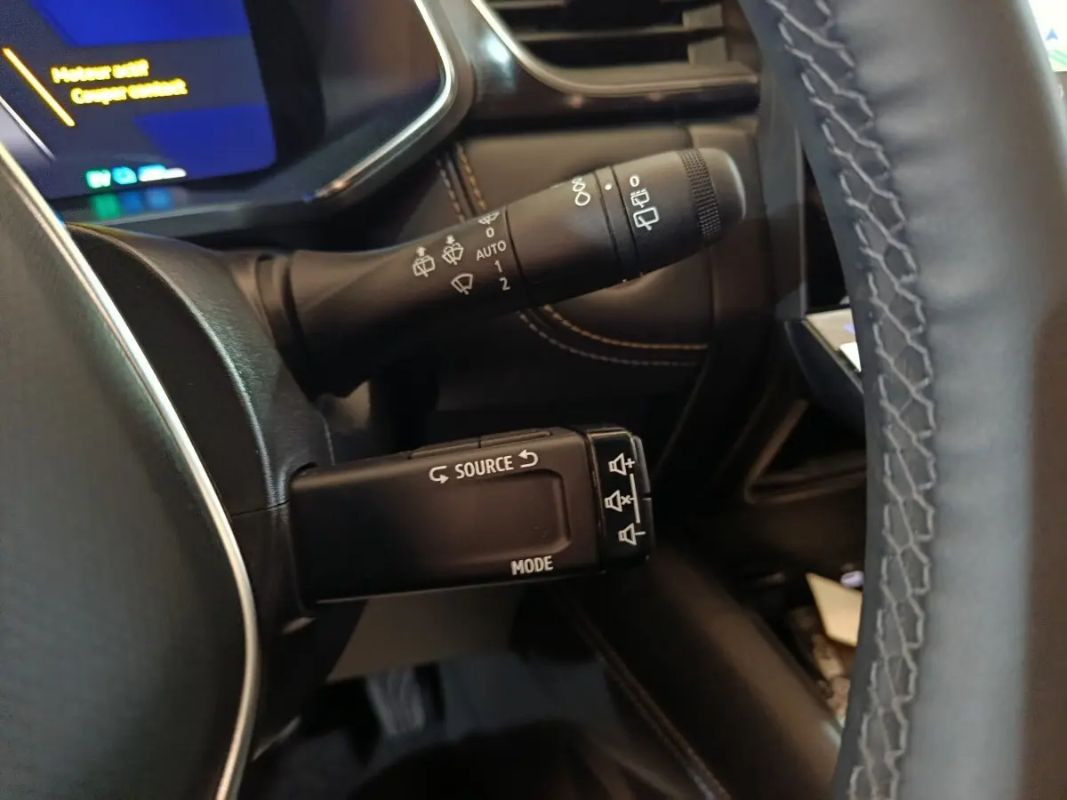 Gros plan sur les commandes au volant noir et les coutures marron du tableau de bord du Renault Symbioz bleu 2025.