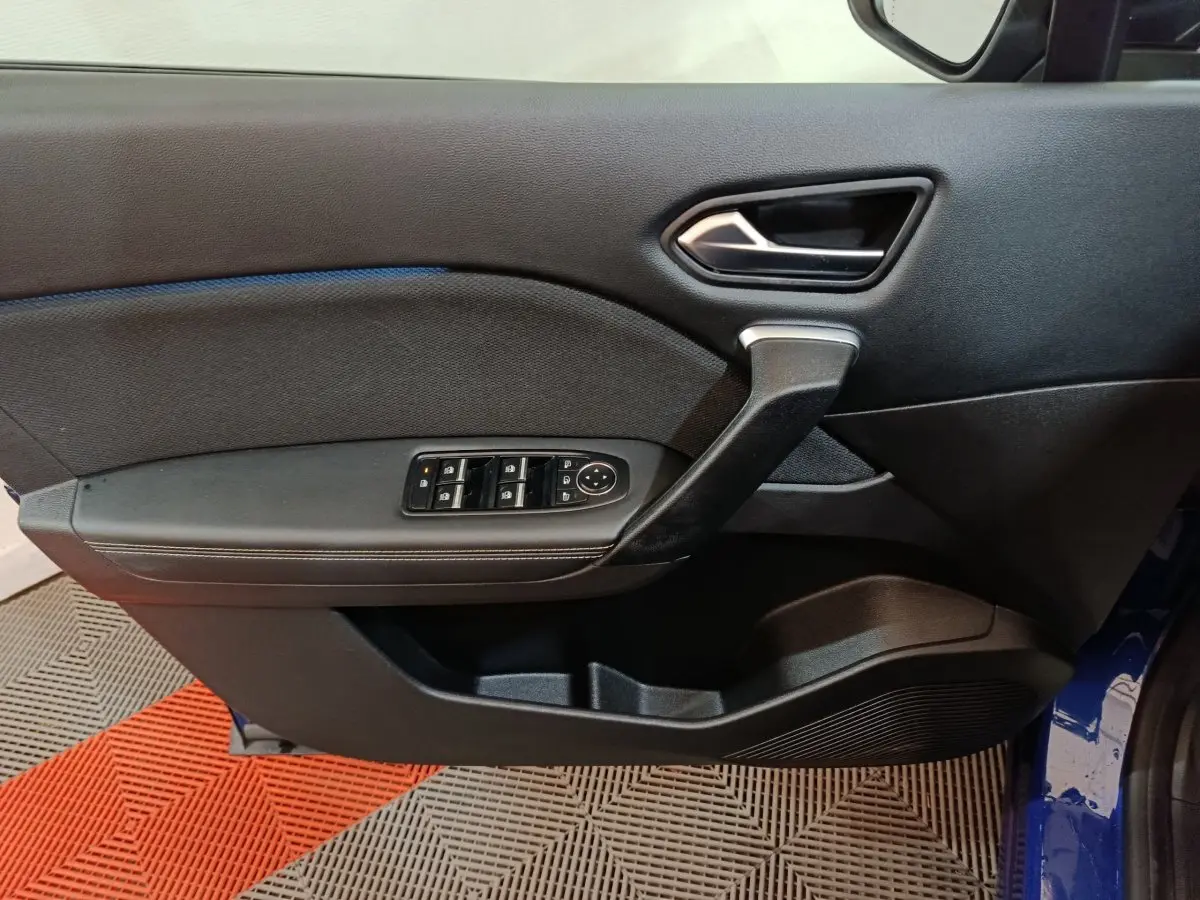 Vue intérieure côté gauche de la porte avant d’une Renault Symbioz bleu, avec commandes électriques et poignée noire.