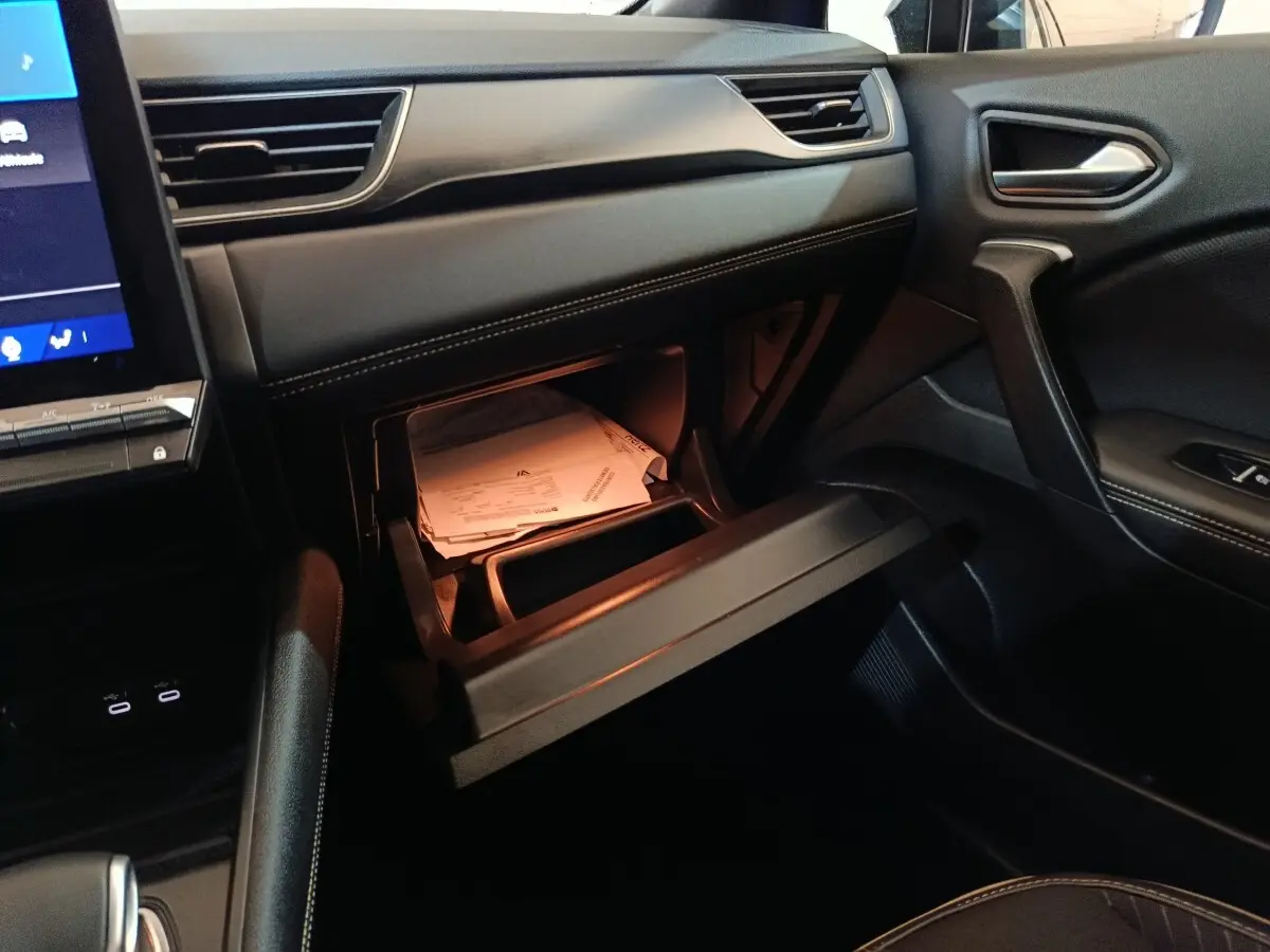 Vue intérieure côté passager du Renault Symbioz 2025 bleu, avec boîte à gants ouverte et documents visibles.
