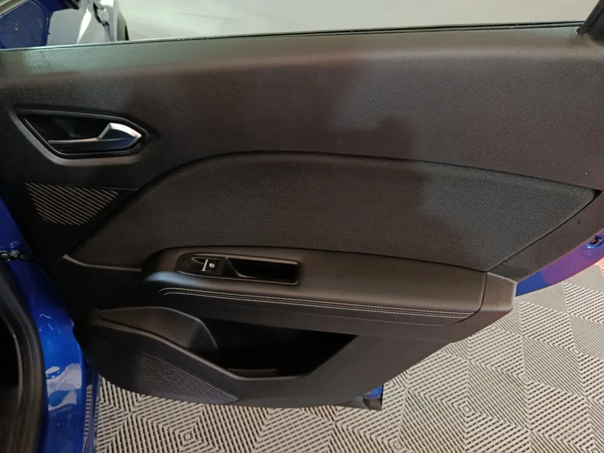Vue intérieure côté gauche de la porte avant bleu Renault Symbioz 2025 avec poignée et commande de vitre noire.