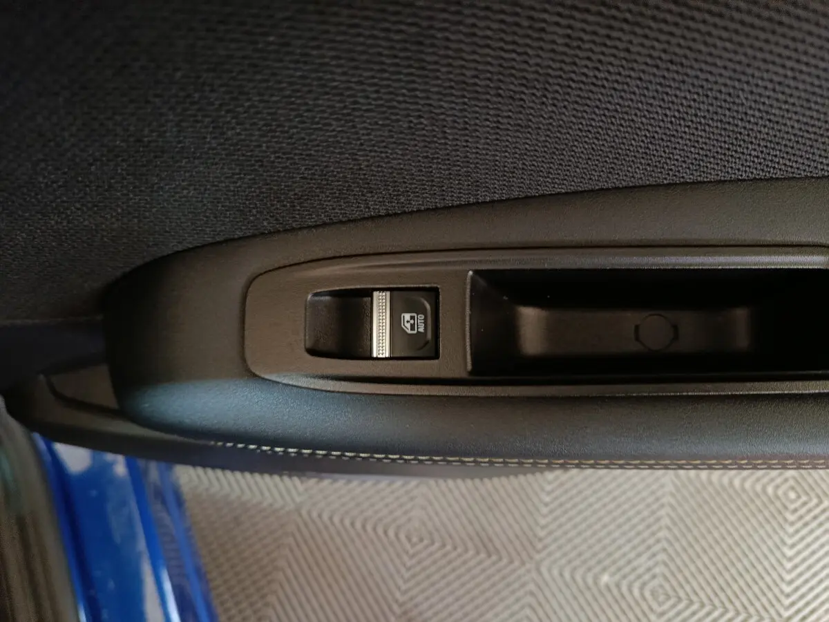 Gros plan sur la commande de lève-vitre côté gauche d'une Renault Symbioz bleu, intérieur tissu noir.