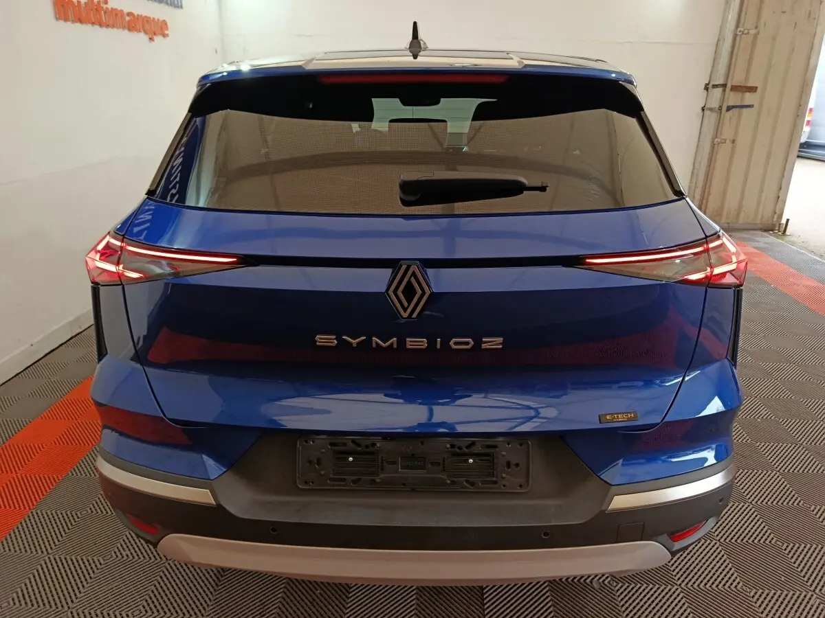 Vue arrière d'une Renault Symbioz bleu avec feux LED fins et logo central distinctif sur un fond intérieur.