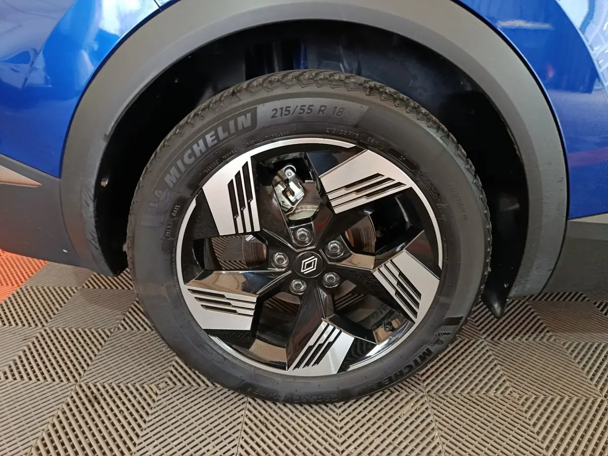 Gros plan sur la roue avant droite du Renault Symbioz bleu, jante alliage noire et argent avec logo Renault central.