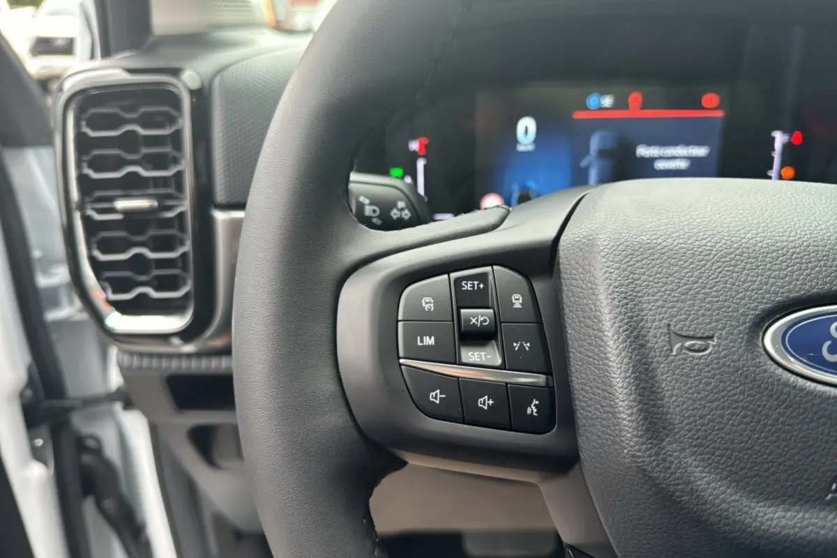 Gros plan sur le volant multifonctions noir du Ford Ranger blanc glacier, avec commandes de régulateur et audio visibles.