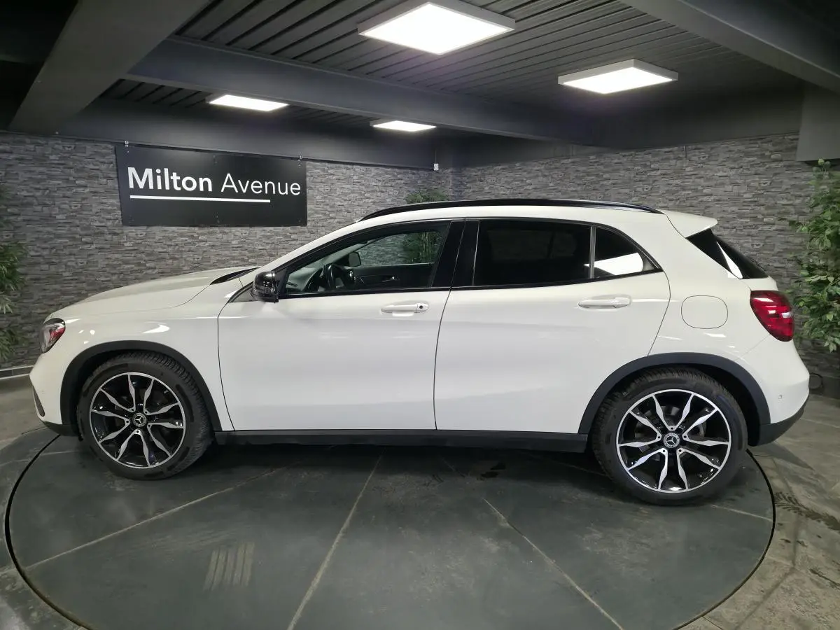 Vue de profil côté gauche d'un Mercedes GLA blanc avec jantes alliage 19 pouces bicolores dans un showroom.