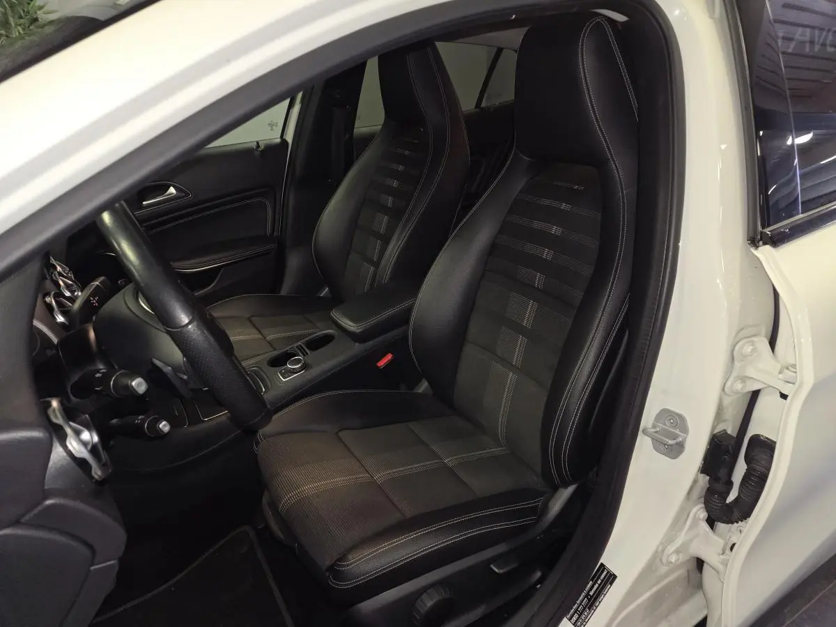 Vue intérieure côté conducteur du Mercedes GLA blanc, mettant en valeur les sièges sport noirs avec surpiqûres contrastées.