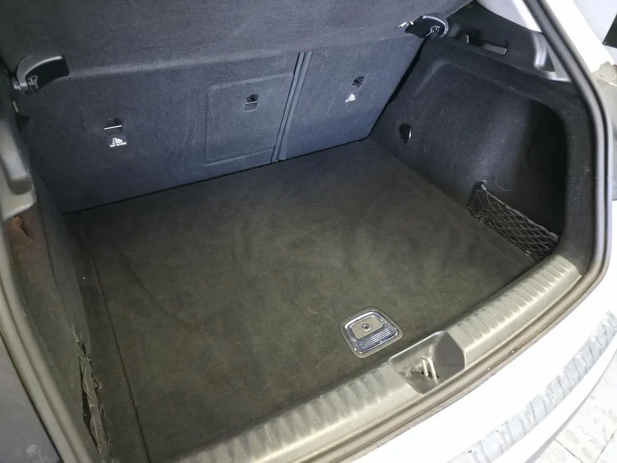 Coffre ouvert vu de l'arrière d'un Mercedes GLA blanc, montrant un espace de chargement propre et tapis noir.