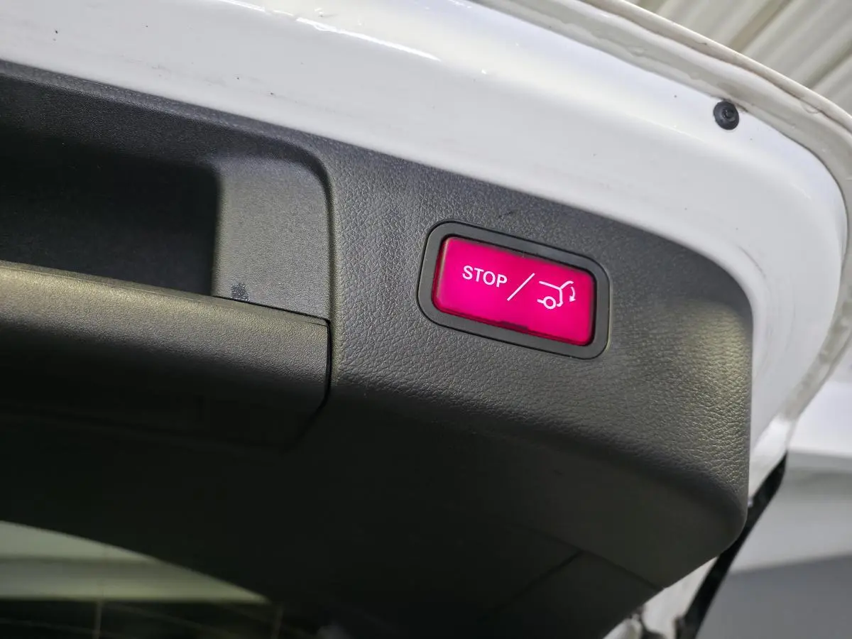 Détail du bouton stop rouge pour hayon électrique sur la partie intérieure du coffre d'un Mercedes GLA blanc.
