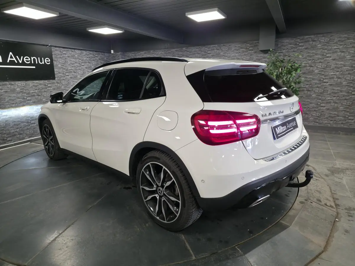 Vue 3/4 arrière droite d'un Mercedes GLA blanc avec jantes alliage noires et attelage démontable en intérieur showroom.