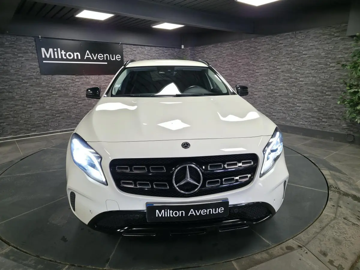Vue avant d'un Mercedes GLA blanc avec calandre noire brillante et phares LED allumés dans un showroom.