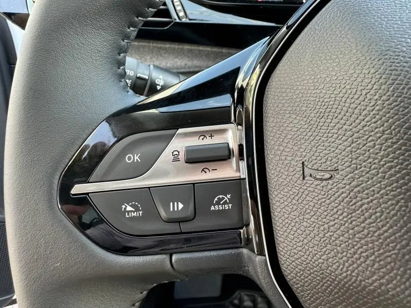 Gros plan sur les commandes du volant côté gauche de la Peugeot 308 bleu, avec boutons de régulateur et limiteur de vitesse.