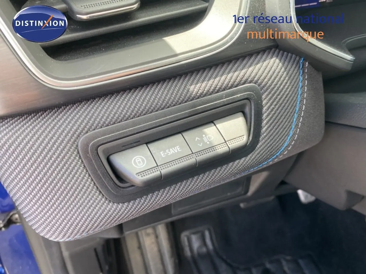 Gros plan sur les commandes E-SAVE et réglage des phares sur la planche de bord en tissu carbone bleu du Renault Symbioz 2025.
