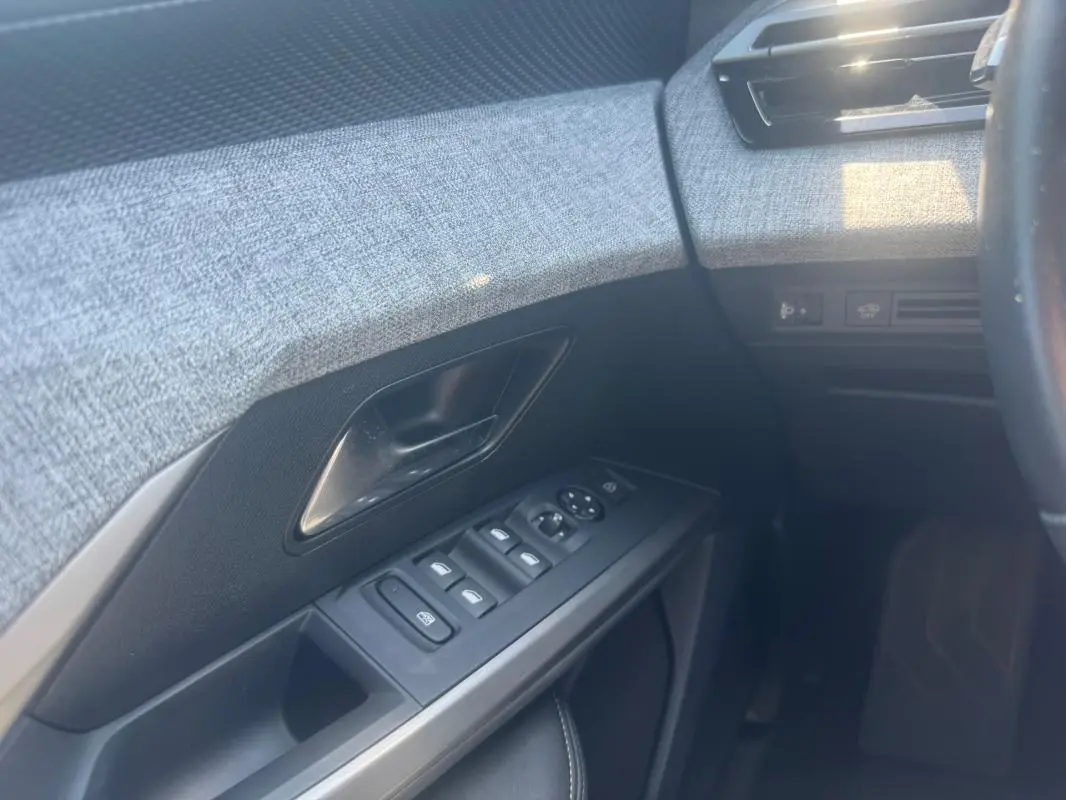 Détail de la porte côté conducteur du Peugeot 5008 Hybrid 2025, montrant les commandes des vitres et la garniture grise texturée.