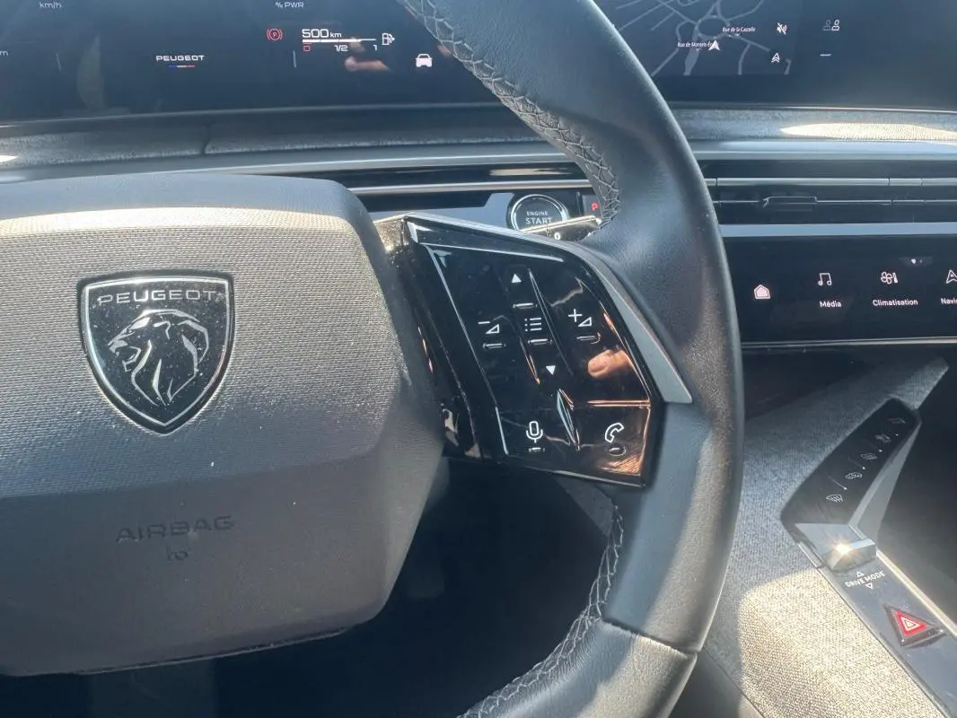 Vue rapprochée du volant noir du Peugeot 5008 Hybrid 2025 avec commandes tactiles et tableau de bord numérique.