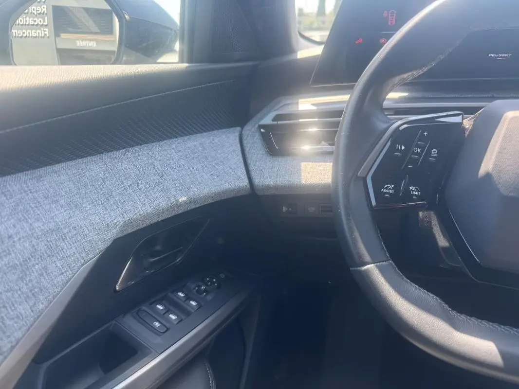 Intérieur du Peugeot 5008 Hybrid 2025, vue côté conducteur sur volant, commandes et panneau de porte gris clair.