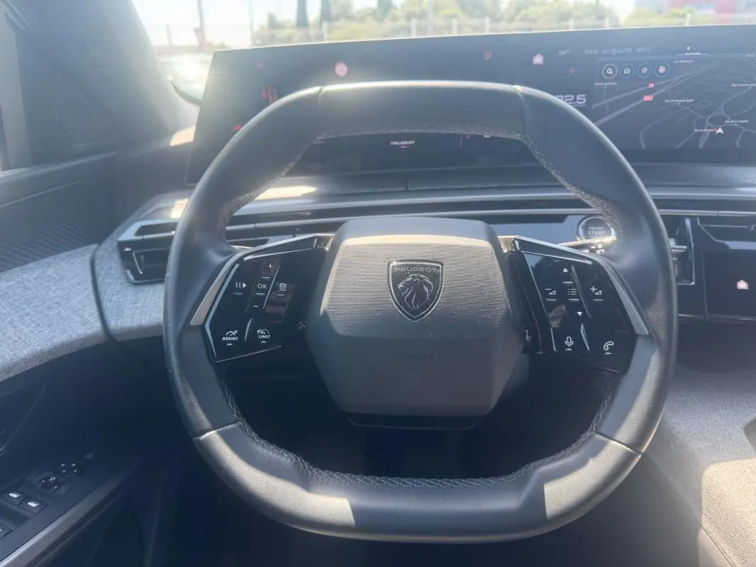 Vue rapprochée du volant cuir noir du Peugeot 5008 Hybrid 2025, avec commandes intégrées et tableau de bord numérique.