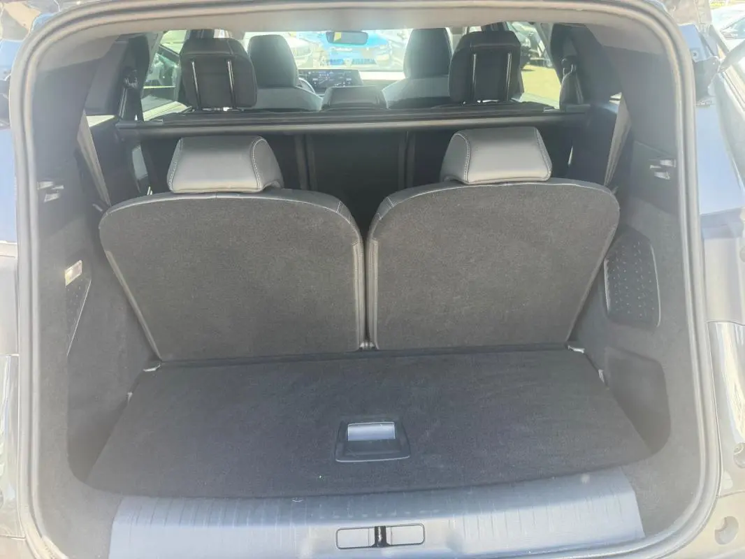 Coffre ouvert vu de l'arrière d'un Peugeot 5008 gris 2025 Hybrid Allure avec sièges arrière relevés.