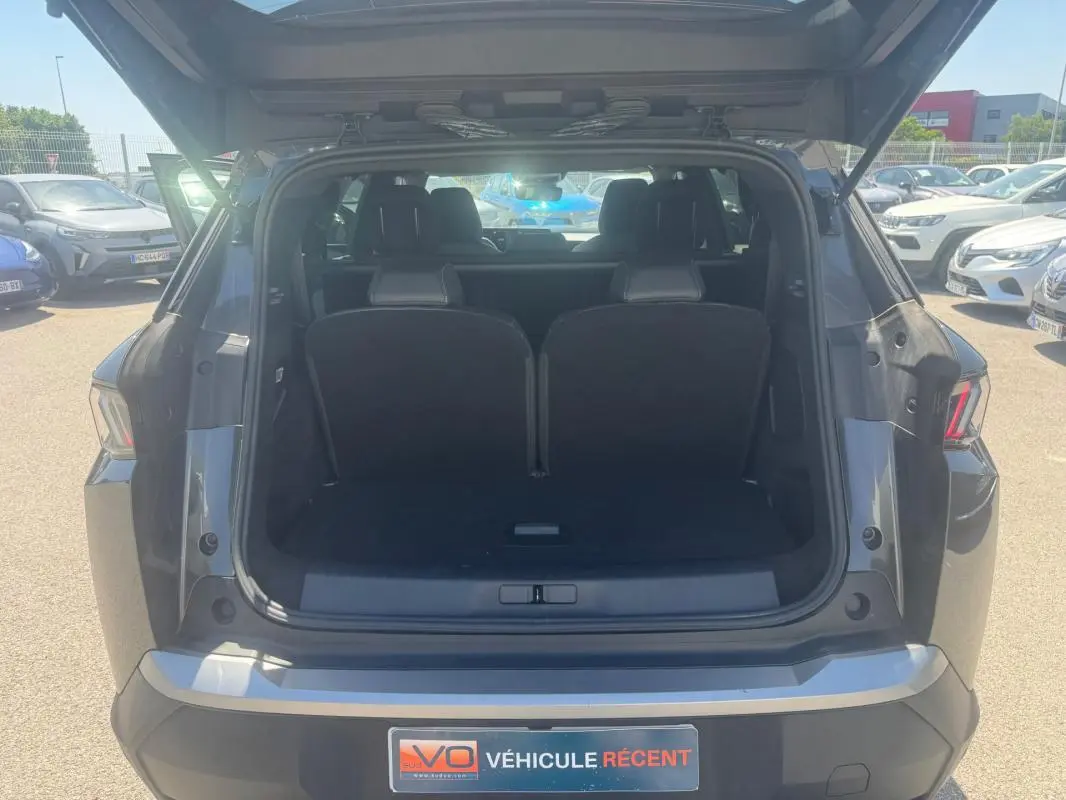 Coffre ouvert vu de l'arrière d'un Peugeot 5008 gris Hybrid 145 ch e-DCS6 Allure 2025 sur parking.